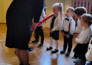 Pani Dyrektor pasuje dziecko na przedszkolaka czerwoną kredką.