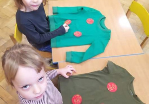 Dzieci naklejają na zielone koszulki ozdobione bombki.