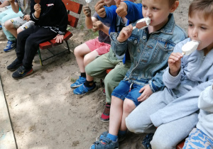 Dzieci siedzą na ławce i jedzą lody