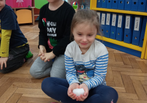 Zdjęcie przedstawia dziewczynkę i chłopca. Dziewczynka trzyma kulkę śniegu w dłoniach.