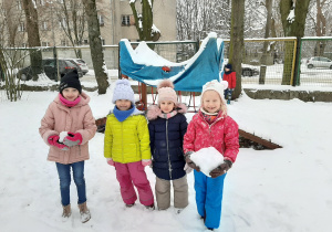 Zdjęcie przedstawia cztery dziewczynki w ogrodzie przedszkolnym. Dwie dziewczynki trzymają kule śnieżne.