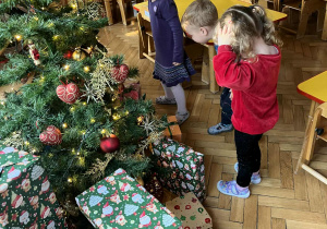 Przedszkolaki oglądają prezenty pod choinką
