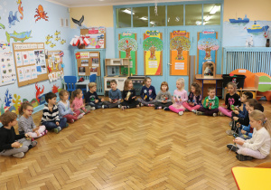 Dzieci siedzą w półkolu z instrumentami: kołatki, grzechotki, tamburyn, talerze, trójkąty.