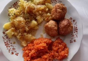 Zdjęcie przedstawia danie obiadowe: ziemniaki, surówka z marchewki i pulpety.
