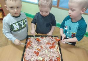 Zdjęcie przedstawia chłopców, którzy nakładają pomidorki koktajlowe na pizzę.