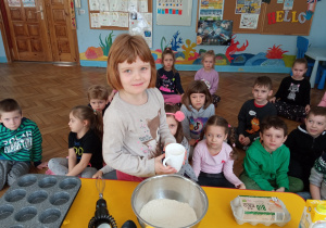 Zdjęcie przedstawia dziewczynkę wsypującą mąkę do miski.