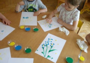 Dzieci malują farbami nizapominajkę.