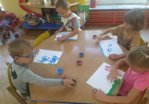 Dzieci odbijają dłonie zamoczone w farbie na papierze.