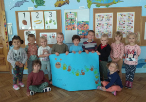 Grupa dzieci prezentuje prace plastyczną - stonoga na niebieskim brystolu.