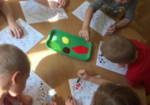 Dzieci malują kropki farbami na liściach.