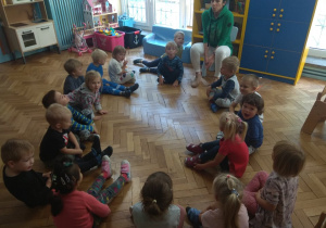 Dzieci siedzą w kole razem z nauczycielem.
