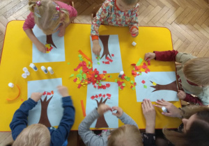 Dzieci wykonują pracę plastyczną jesienne drzewo, wydzierając kolorowy papier.