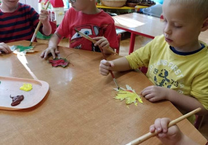 Dzieci malują farbami liście.