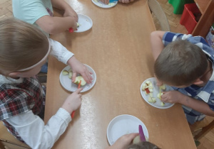 Dzieci kroją jabłka do sałatki owocowej.