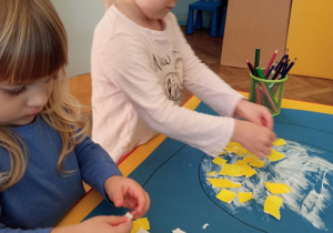 Dzieci wyklejają jajko żółtym papierem.