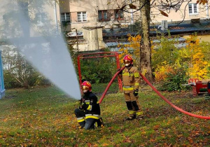 Strażacy demonstrują dzieciom gaszenie pożaru wodą.