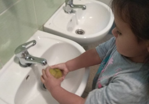 Dziewczynka myje jabłko w umywalce.