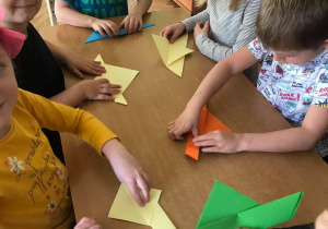 Dzieci składają kolorowy papier tworząc ptaki z origami.