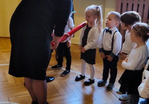 Pani Dyrektor pasuje dziecko na przedszkolaka czerwoną kredką.