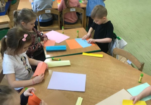 Dzieci składają papier techniką origami tworząc kredki.