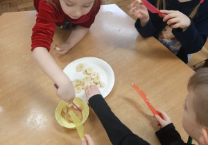 Dzieci smarują plastry banana masłem orzechowym.