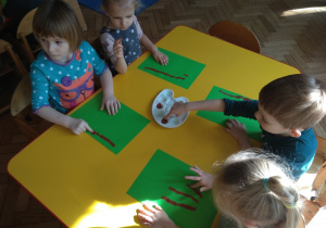 Dzieci malują palcem i brązową farbą gałęzie.