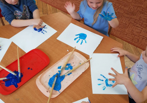 Dzieci odbijaja soje dłonie w niebieskiej farbie.