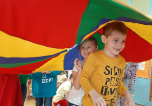 Dwoje dzieci stoją pod chustą animacyjną w kolorach: czerwony, żółty, niebieski, zielony.
