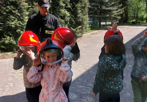 Dzieci mierzą hełm strażacki.