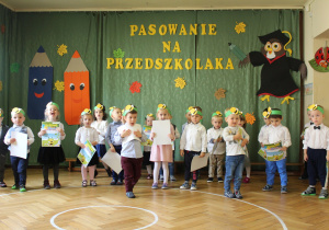 Zdjęcie przedstawia grupę dzieci ubranych na galowo w opaskach z symbolem pszczoły.