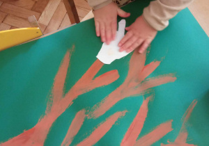 Dziewczynka przykleja odrysowaną i wyciętą dłoń na plakacie z drzewem.