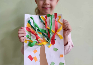 Dziewczynka i jej praca plastyczna jesienne drzewo.