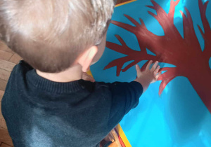Chłopiec odbija rączkę pomalowaną farbą na plakacie z drzewem.