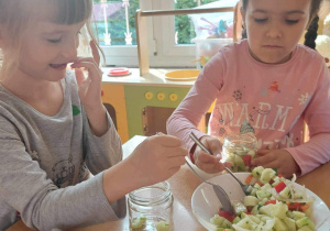 Dzieci przygotowują sałatkę warzywną w słoiku.