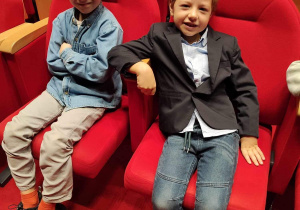 Dzieci siedzą w teatrze na czerwonych krzesłach.