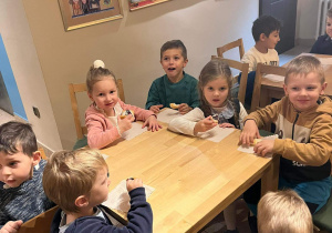 Dzieci jedzą ciasteczka przy stolikach.