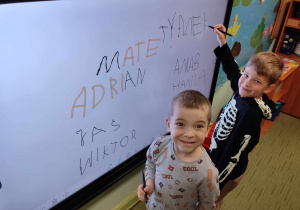 Dzieci piszą swoje imię na tablicy mutlimedialnej.