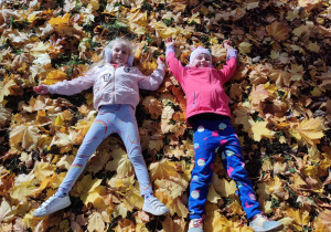 Dziewczynki leżą na jesiennych liściach.
