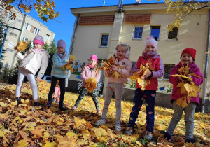 Dziewczynki podrzucają jesienne liście do góry.