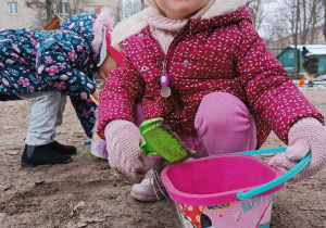 Dziewczynka bawi się łopatka i wiaderkiem w ogrodzie przedszkolnym.