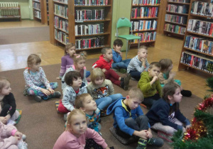 Dzieci siedzą ba dywanie w bibliotece.