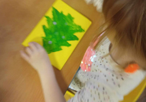 Dzieci malują choinkę zieloną farbą.