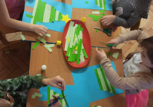 Dzieci układają choinkę z pociętych zielonych pasków.
