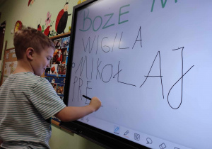 Chłopiec pisze na tablicy wyraz prezent.