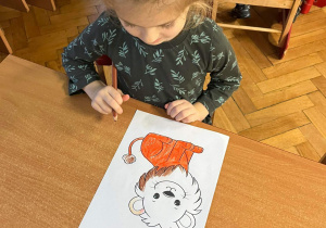 Dziewczynka koloruje rysunek lwa.