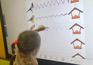Dziewczynka rysuje po śladzie drogę ptaka do karmnika na dużym ekranie.