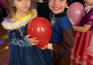 Dziewczynka i chłopiec tańczą z balonem.